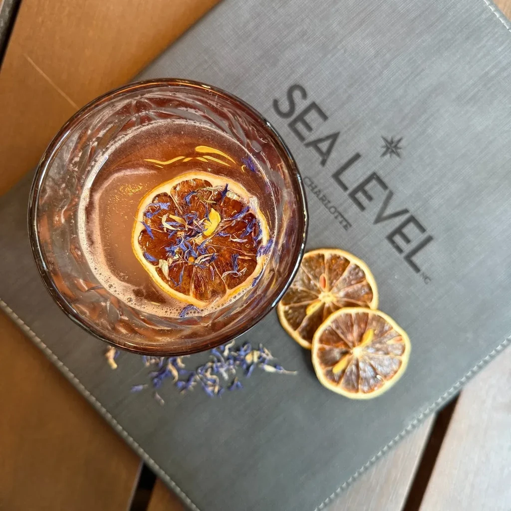 Amber cocktail with dried citrus and blue petals on a "Sea Level" menu.