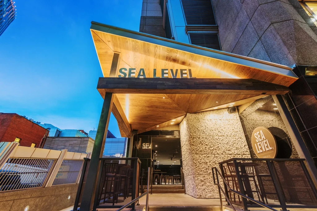SEA LEVEL building entrance with angular wooden canopy and outdoor seating.