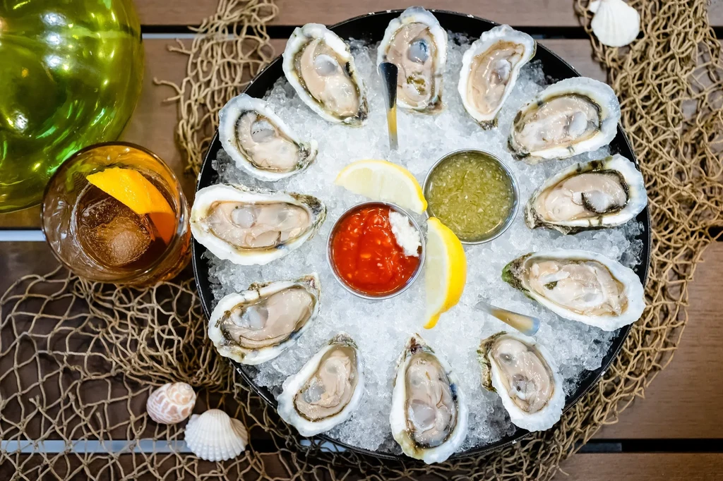 Overhead: shucked oysters on ice with sauces, lemon, and an amber drink.