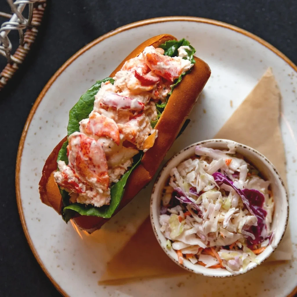 Toasted lobster roll with creamy meat and colorful coleslaw on a plate.