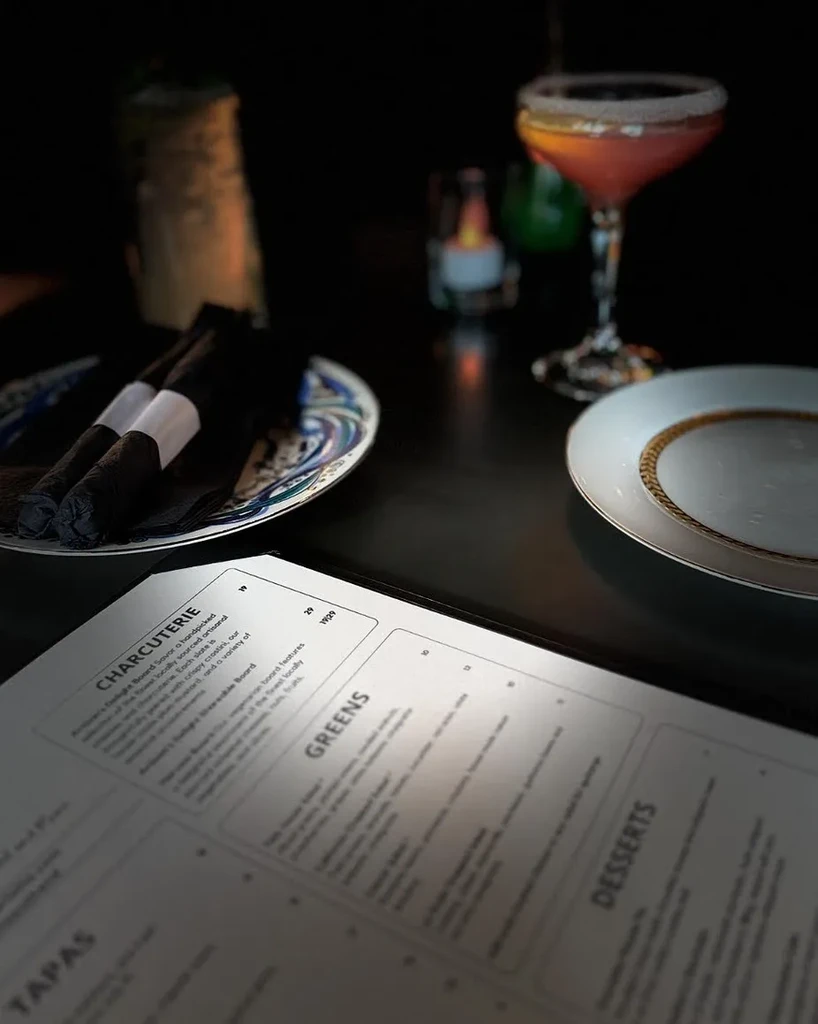 Dimly lit restaurant table with an open menu, cocktail, and napkins.