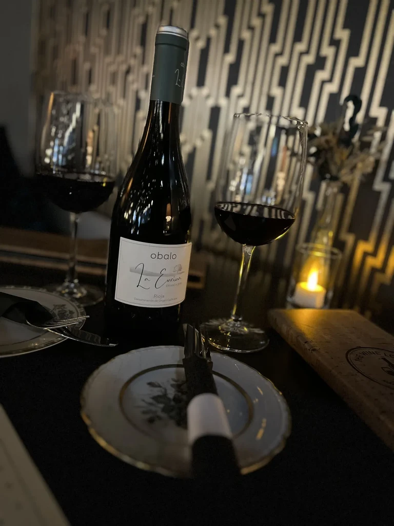 Dimly lit restaurant table with red wine bottle, two glasses, and candle.
