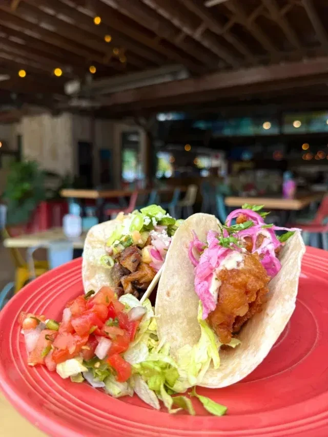 Two vibrant tacos with meat and fish on a bright red plate.
