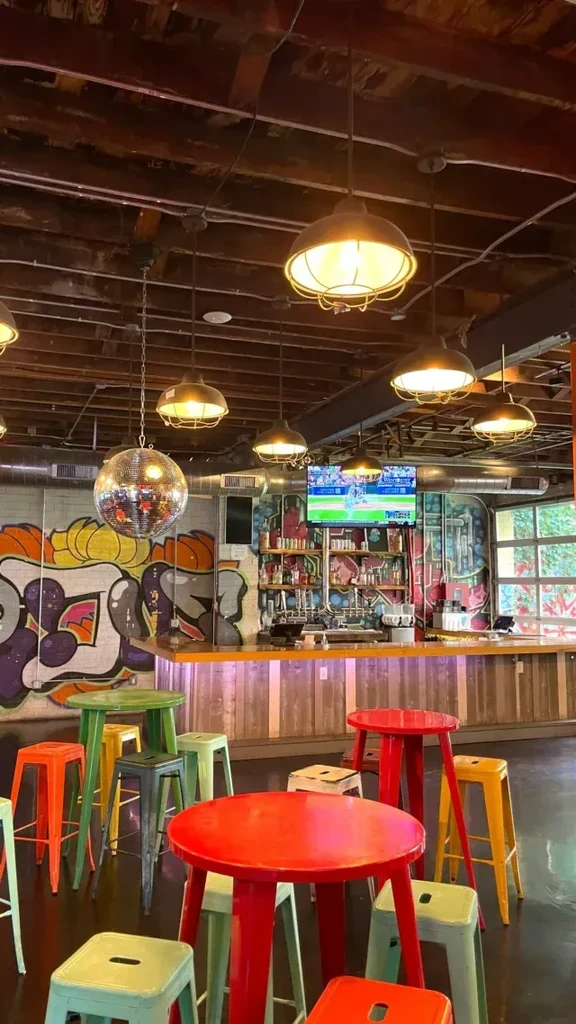 Eclectic bar interior: disco ball, graffiti, industrial lighting, colorful high-tops.