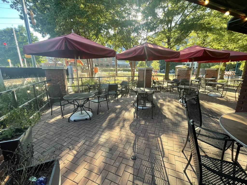 Empty outdoor patio with metal tables, chairs, maroon umbrellas, and brick.
