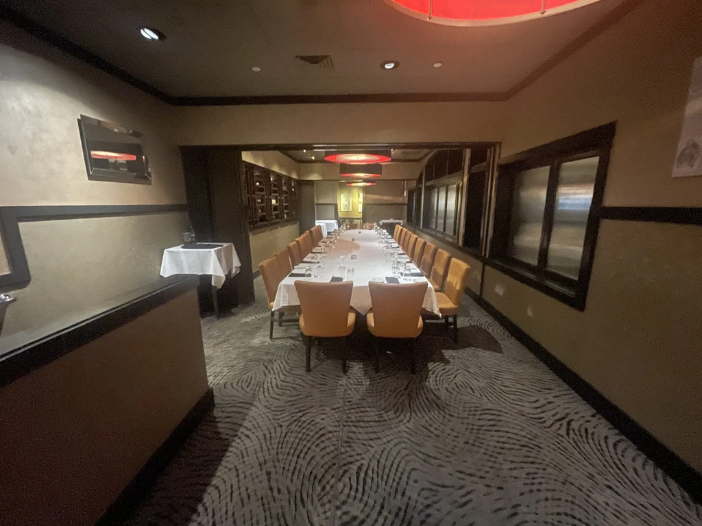 Dimly lit private dining room with long table and orange chairs.
