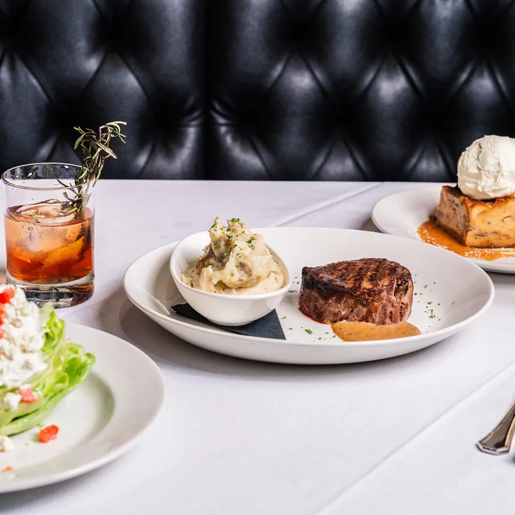 Grilled steak, salad, cocktail, and dessert on an upscale restaurant table.