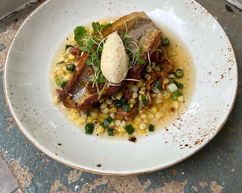 Crispy-skinned pan-seared fish on succotash with quenelle and microgreens.