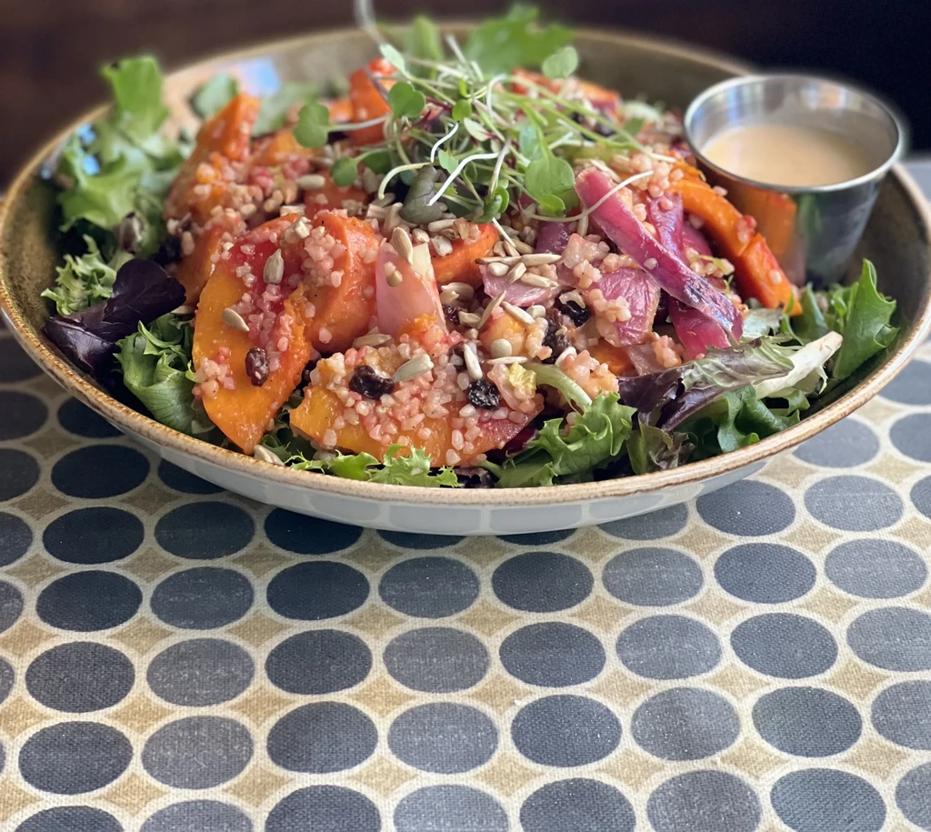 Vibrant salad in a bowl with greens, roasted vegetables, grains, and dressing.
