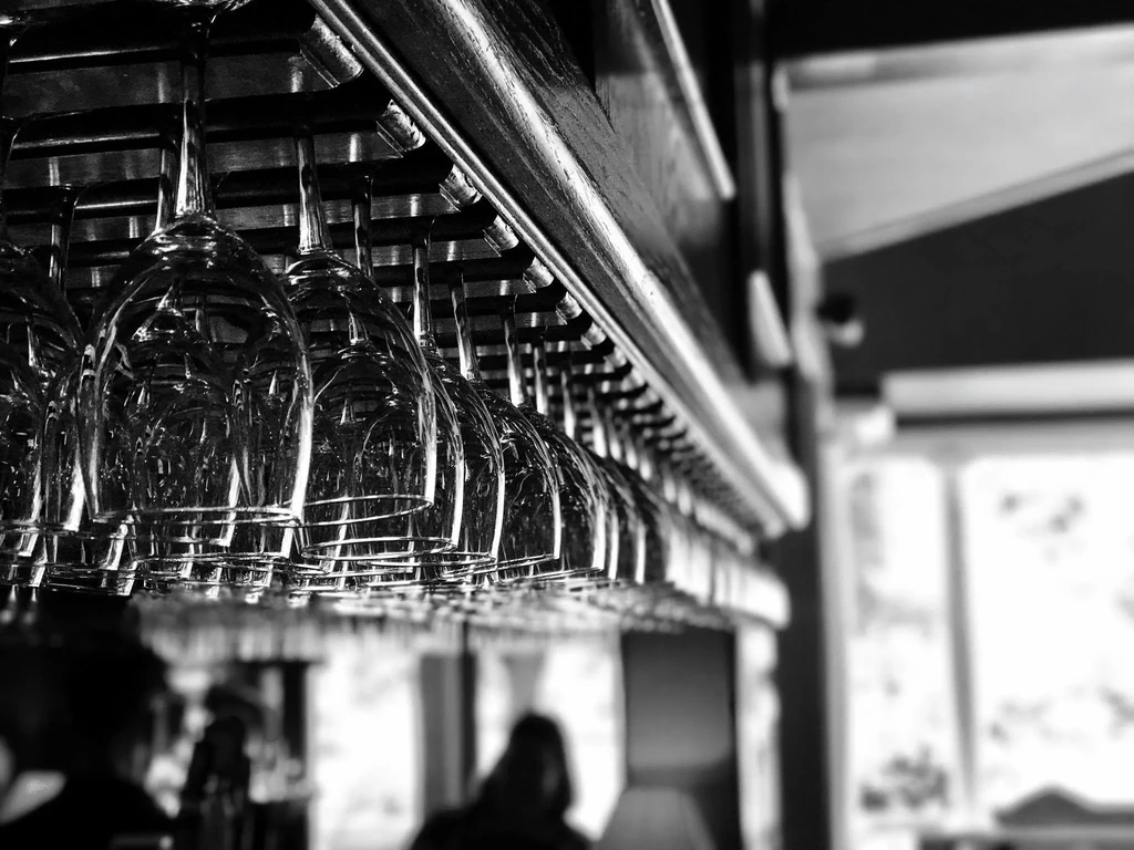 Black and white photo of sharp, hanging wine glasses, blurred bar interior.