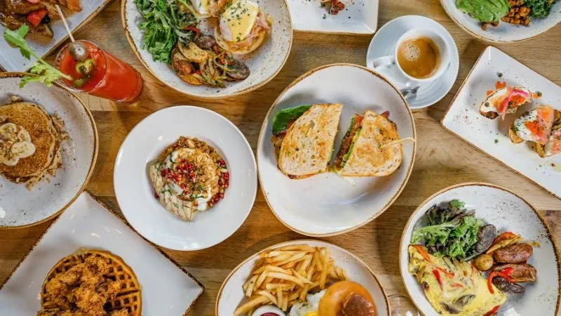 Overhead shot of a wooden table laden with diverse brunch food and drinks.