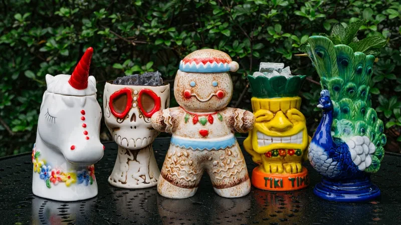 Five whimsical ceramic mugs: unicorn, skull, gingerbread, tiki, and peacock.