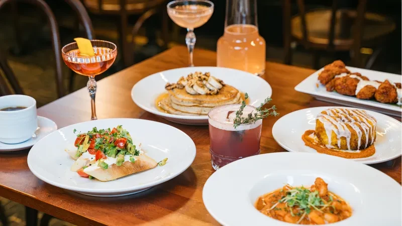 Diverse food and drinks spread on a wooden restaurant table.