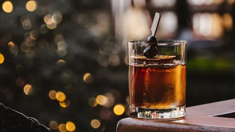 Amber cocktail with citrus, cherries, and ice on a wooden surface.