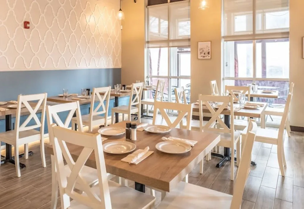 Well-lit modern restaurant interior with light wood tables and X-back chairs.