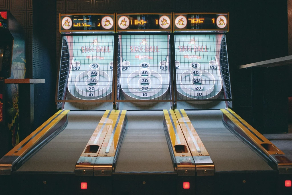 Side-by-side Skee-Ball machines with jester icons in a dimly lit arcade.