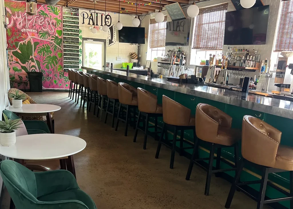 Vibrant Cypress Drinkery interior with dark green bar and tropical mural.