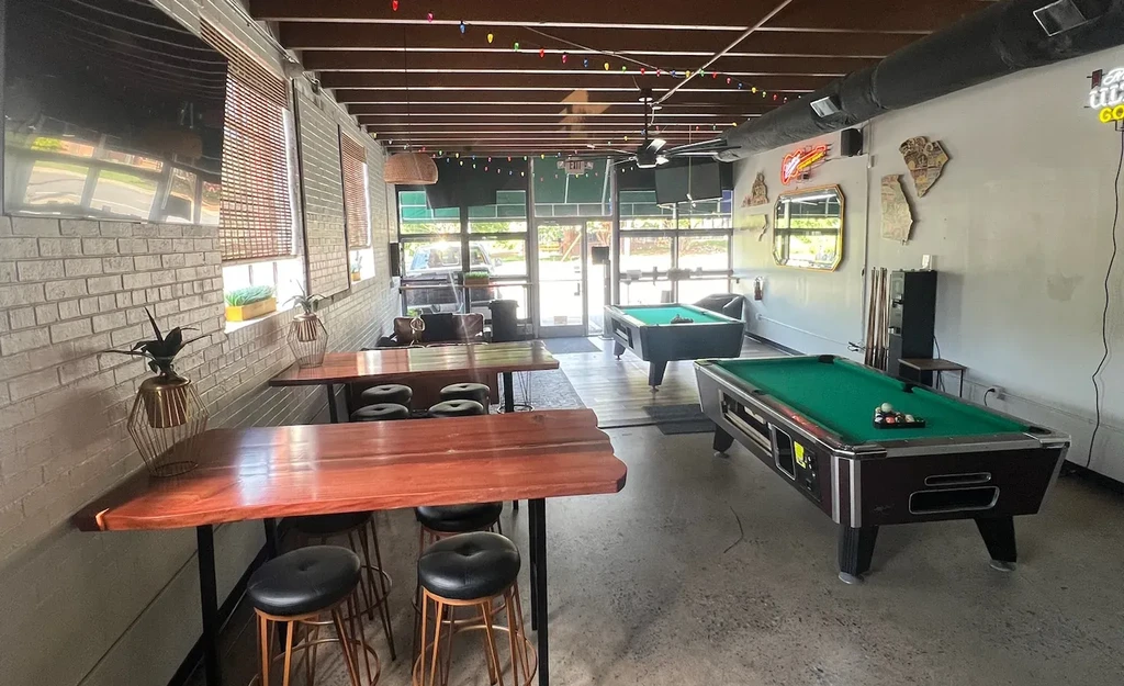 Casual bar interior with two pool tables and festive lights.
