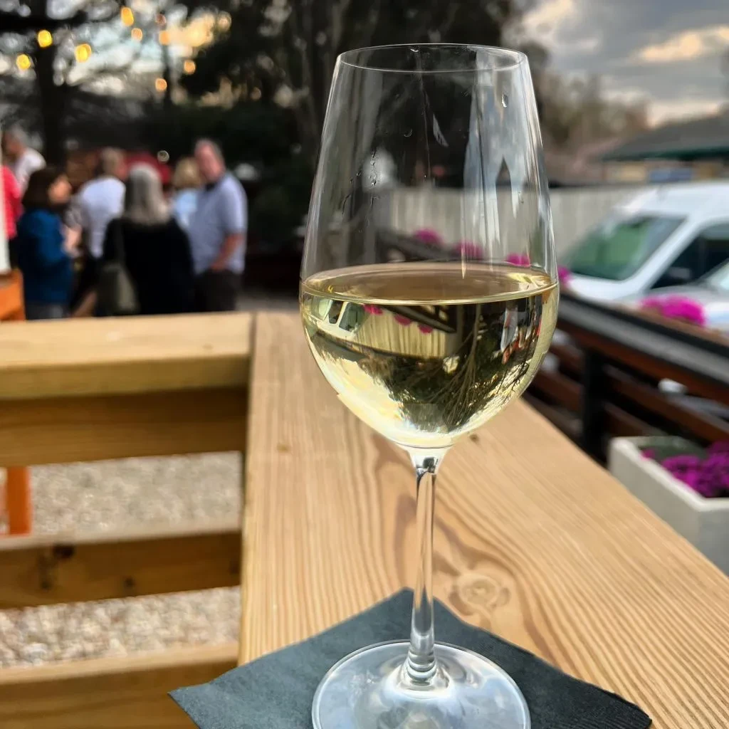 Wine glass on wooden railing, blurred outdoor social setting.