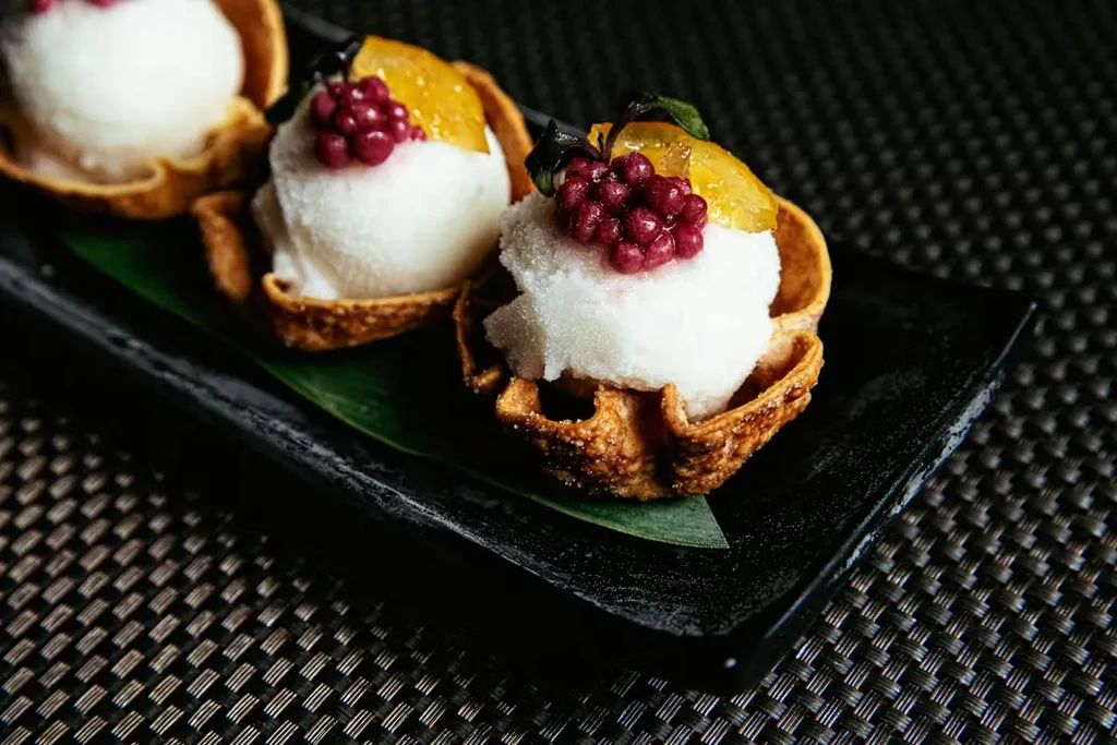 Three elegant waffle cup desserts with sorbet, red berries, and candied peel.