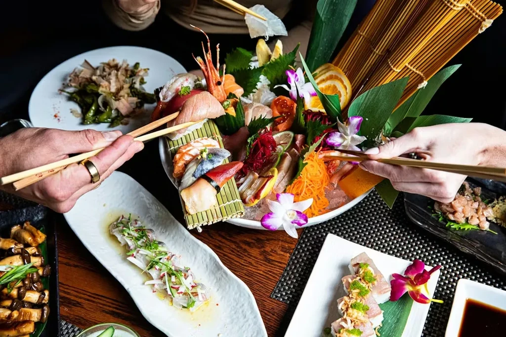 Elaborate Japanese sushi and sashimi platter, other dishes, and hands eating.