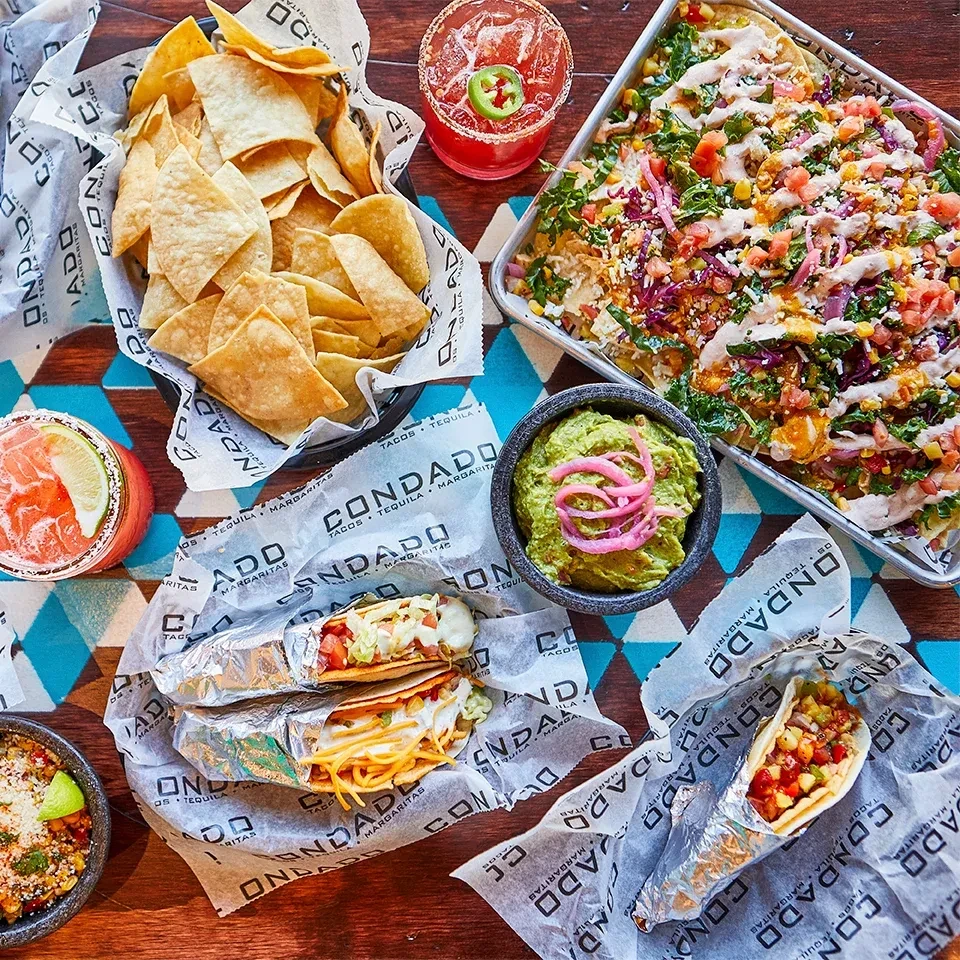 Vibrant overhead view of Mexican tacos, nachos, chips, and drinks.