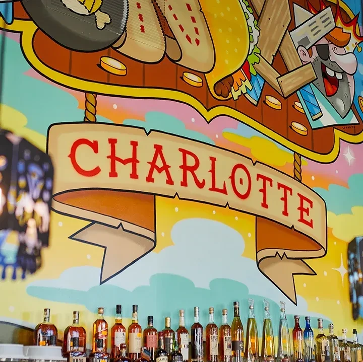 Whimsical bar mural, "CHARLOTTE" banner, and a display of liquor bottles.