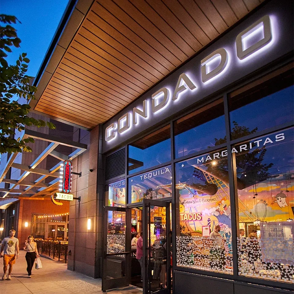 Condado restaurant exterior at dusk, illuminated with signs and visible patrons.