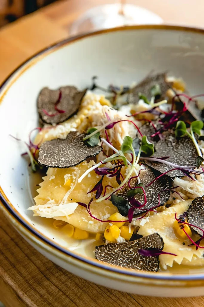 Close-up of golden scalloped pasta, black truffle, corn, and microgreens.