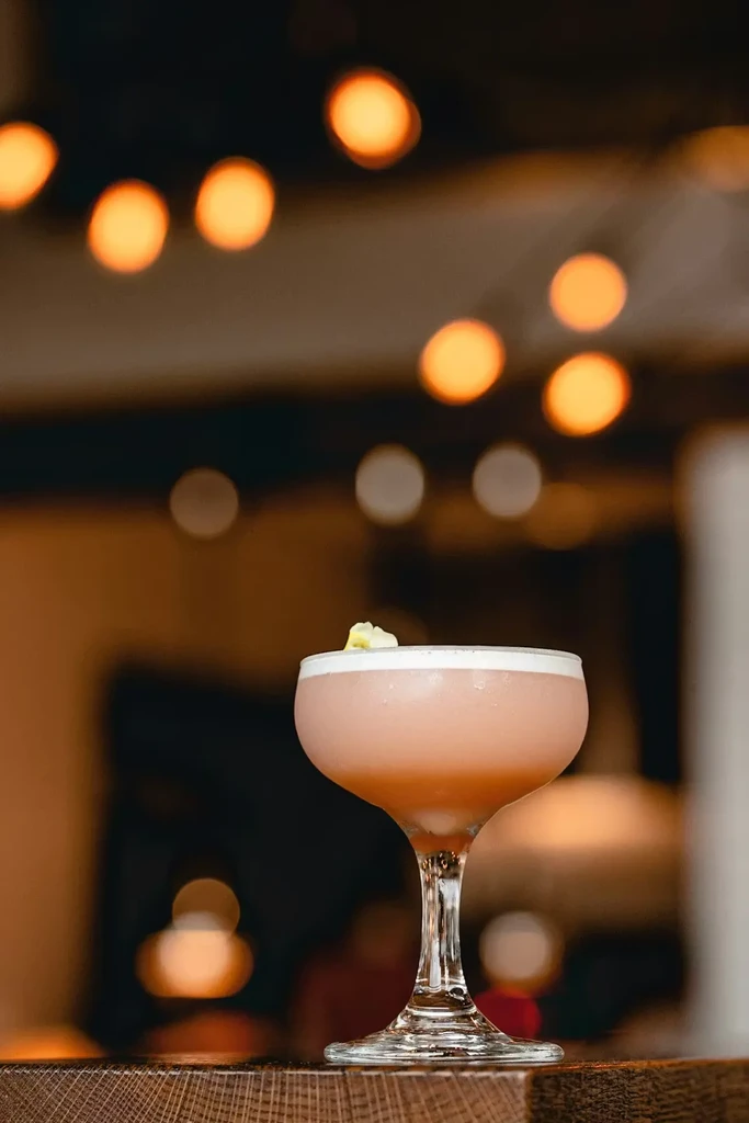 Pink foamy cocktail in a frosted coupe glass on a wooden surface.
