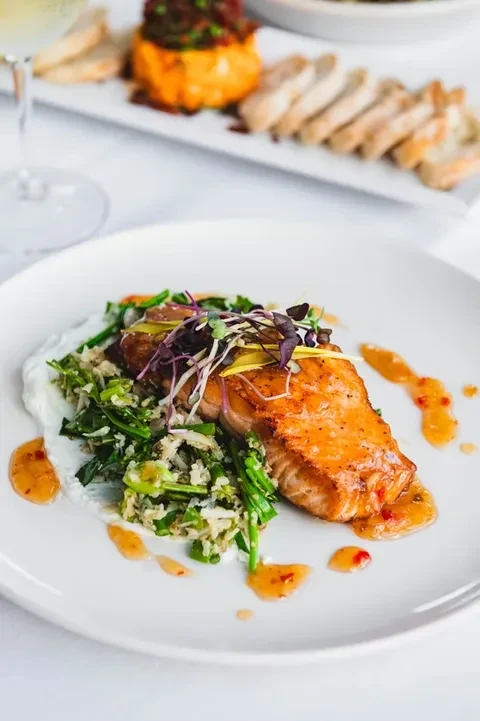 Plated salmon with microgreens, vegetables, and creamy and orange sauces.
