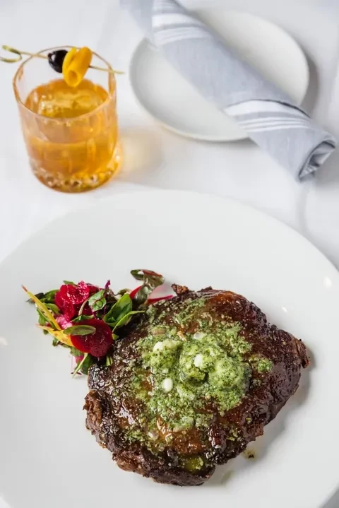 Top-down view: Steak with melting green butter, mixed greens, cocktail.