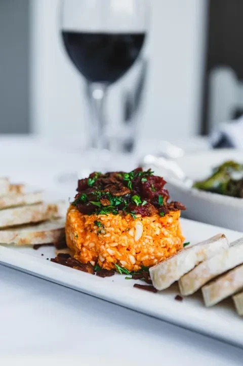 Plated orange grain dish with dark bits, herbs, toasted bread.