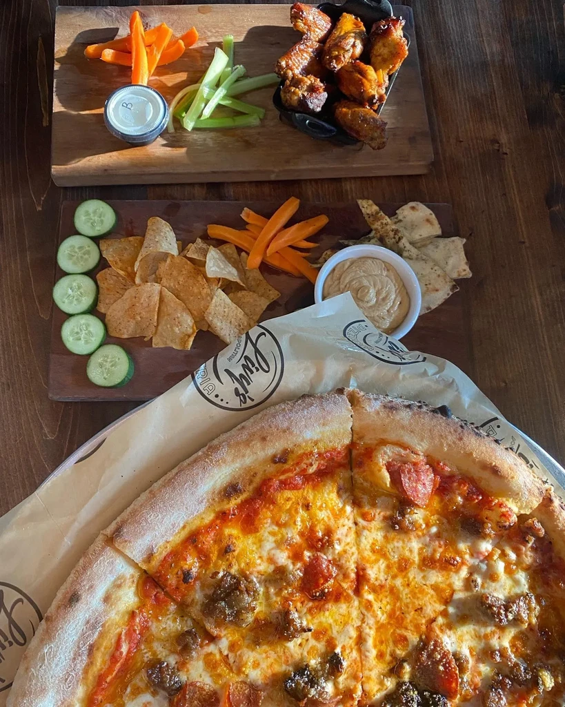 Overhead spread of pizza, wings, chips, and vegetables on wooden boards.