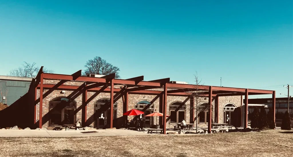 Sunny brick building with red pergola shading patio picnic tables.
