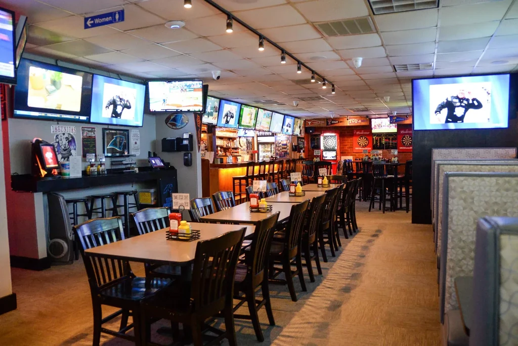 Well-lit, empty sports bar with tables, bar, dartboards, and TVs.