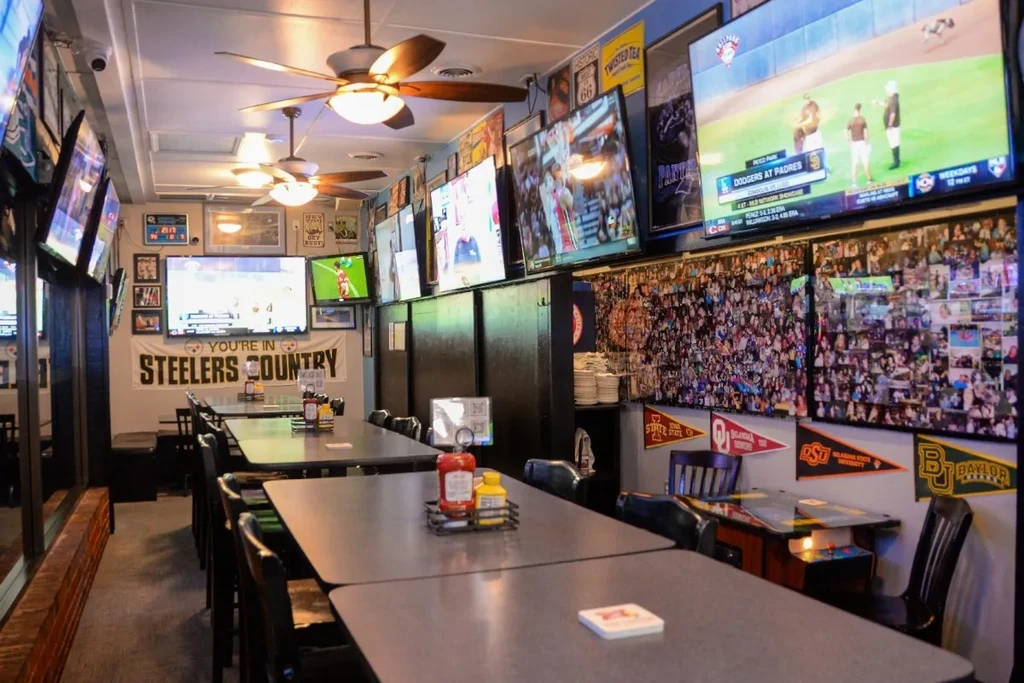 Sports bar interior with many TVs showing games, sports banners, and a photo collage.