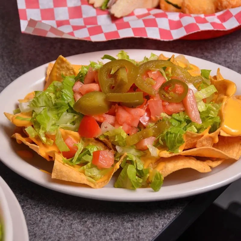 Plate of nachos with melted cheese, shredded lettuce, diced tomatoes, jalapeños.