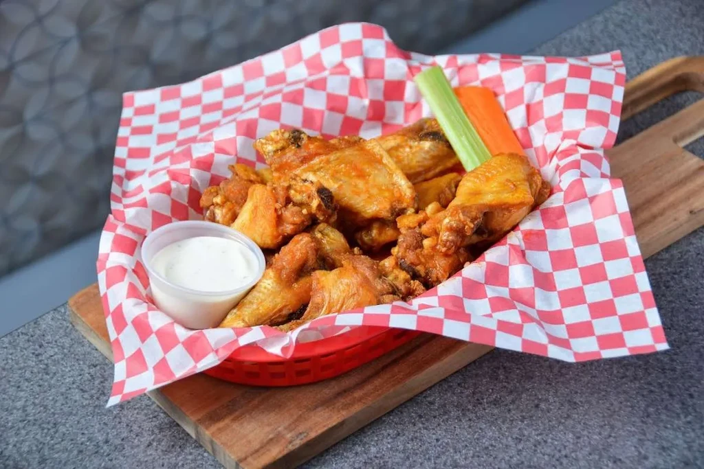 Red basket of crispy chicken wings, dip, celery, and carrot.