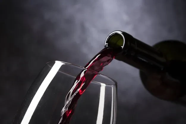 Dark red wine pours from bottle into clear wine glass.
