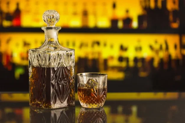 Crystal decanter and glass of amber liquid with ice in a bar.