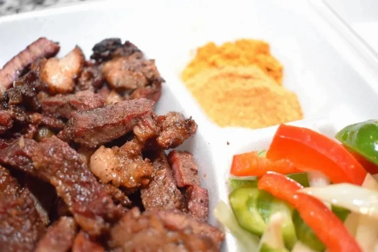 Partitioned plate with grilled meat, red condiment, bell peppers, and onions.