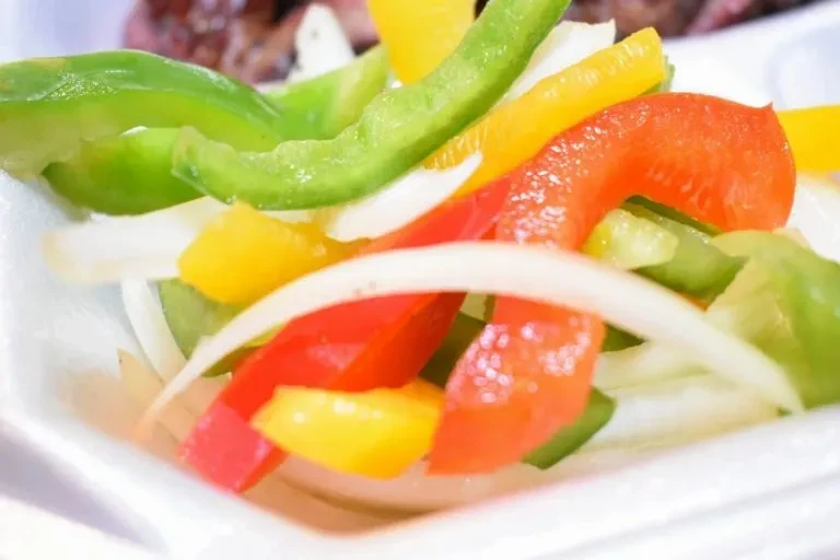 Sliced green, yellow, red bell peppers and onions in a white container.