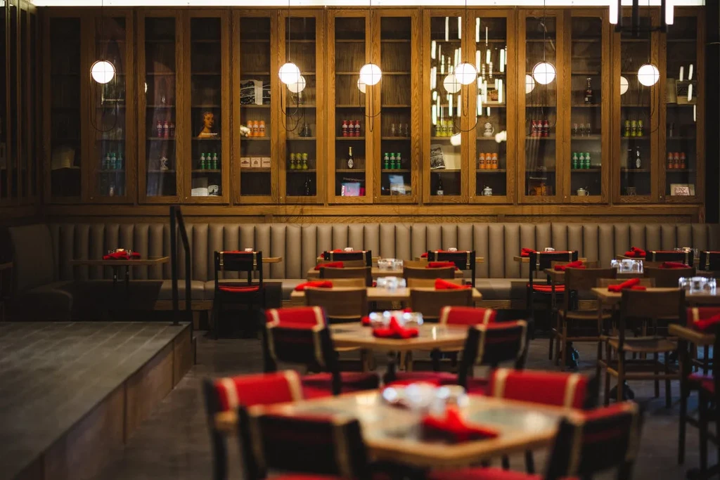 Empty restaurant interior with brown booth, lighted cabinets, and red chairs.