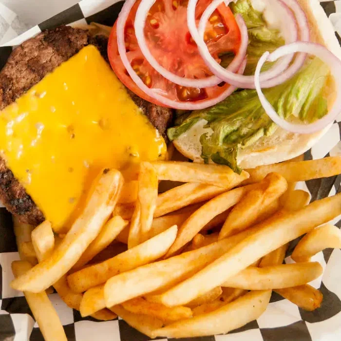 A close-up cheeseburger with fries, served in a checkered basket.