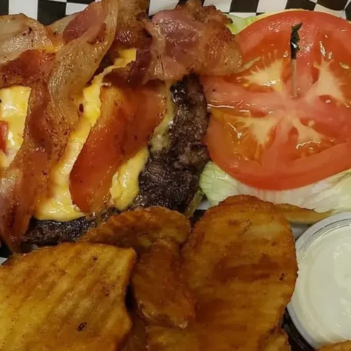 Close-up of bacon cheeseburger, waffle fries, and white dipping sauce.