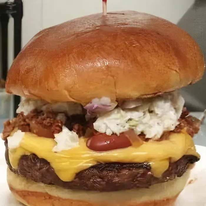 Loaded burger with brioche bun, patty, melted cheese, chili, and coleslaw.