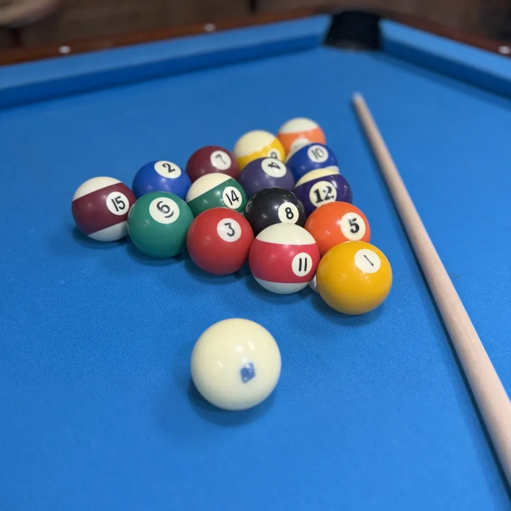 Racked billiard balls on a blue felt pool table with a cue stick.