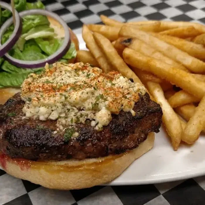 Plate of gourmet burger with crumbly cheese, herbs, and french fries.