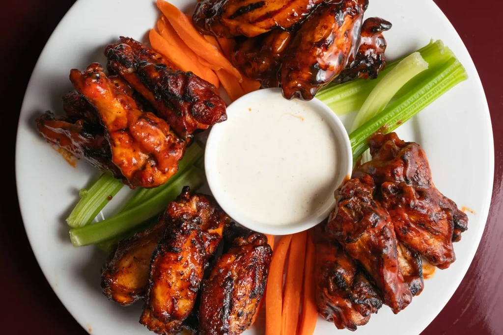 Overhead: glazed chicken wings, creamy dip, carrot, and celery sticks.